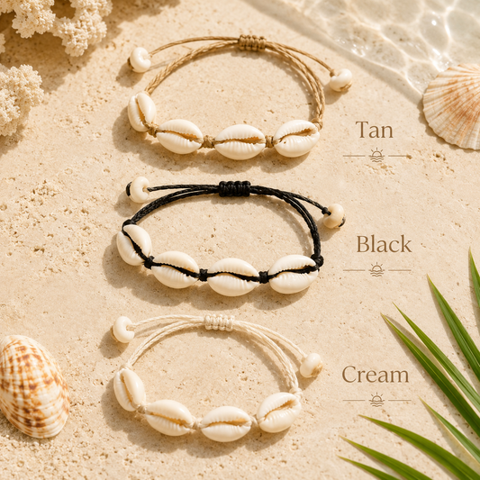 Three braided shell bracelets arranged on a sandy surface with seashells and palm leaves. The bracelets are labeled Tan, Black, and Cream, showing the different braid colors while maintaining the same shell design.