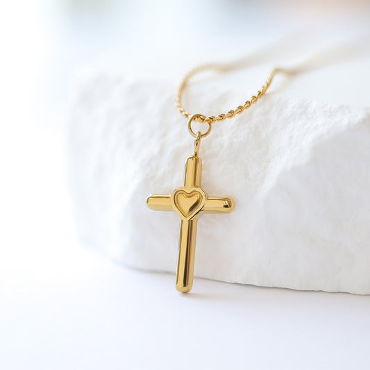 Gold cross necklace with a heart detail on a white background