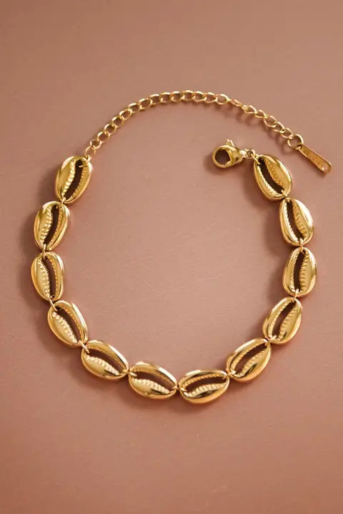 Gold bracelet with shell-like beads on a brown background