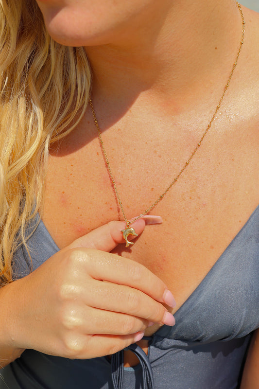 Close-up of a woman wearing a gold necklace with a dolphin pendant.
