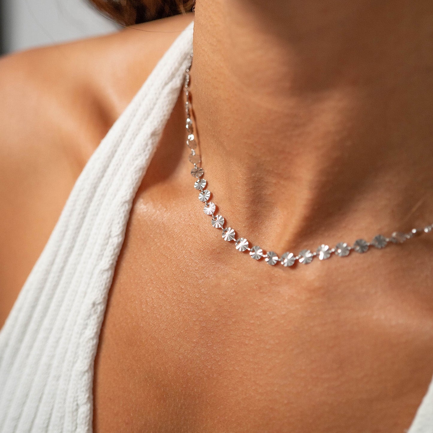 Close-up of a woman in a white halter top wearing a silver necklace with mini suns