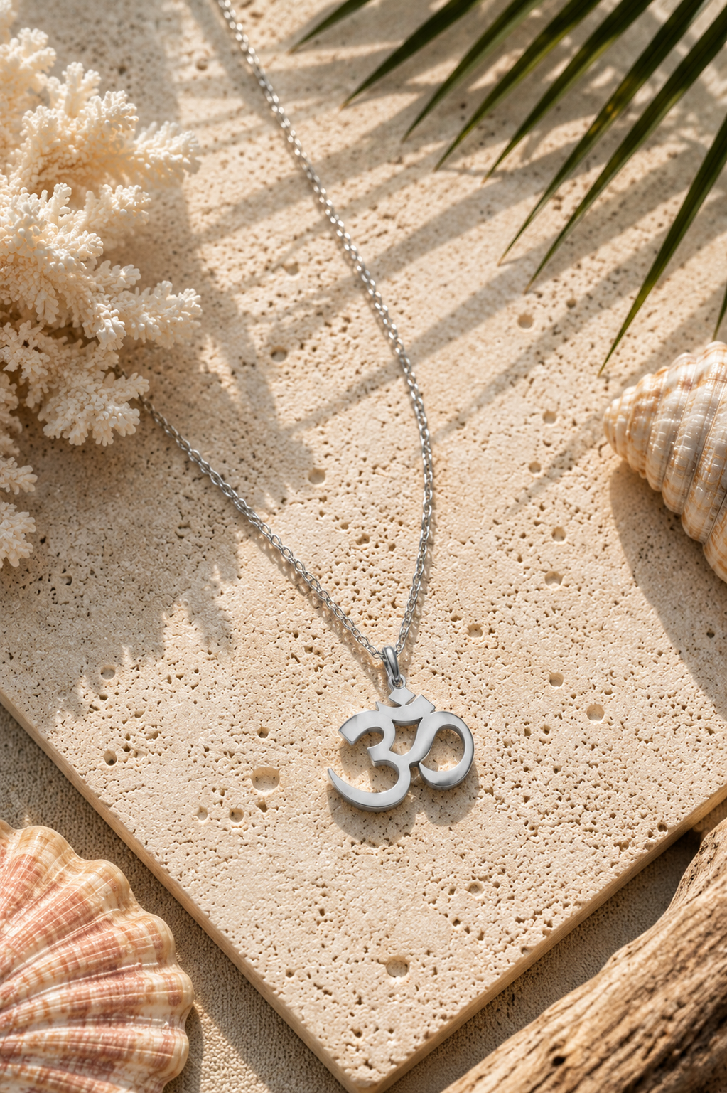 Silver chain with Om symbol lying on cream background near shells.