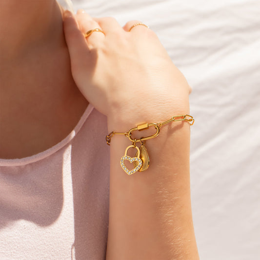Gold bracelet with heart-shaped padlock charms on a person's wrist against a light background