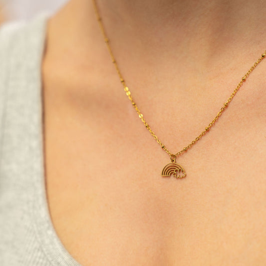 Gold necklace with a rainbow pendant on a person wearing a light-colored top.