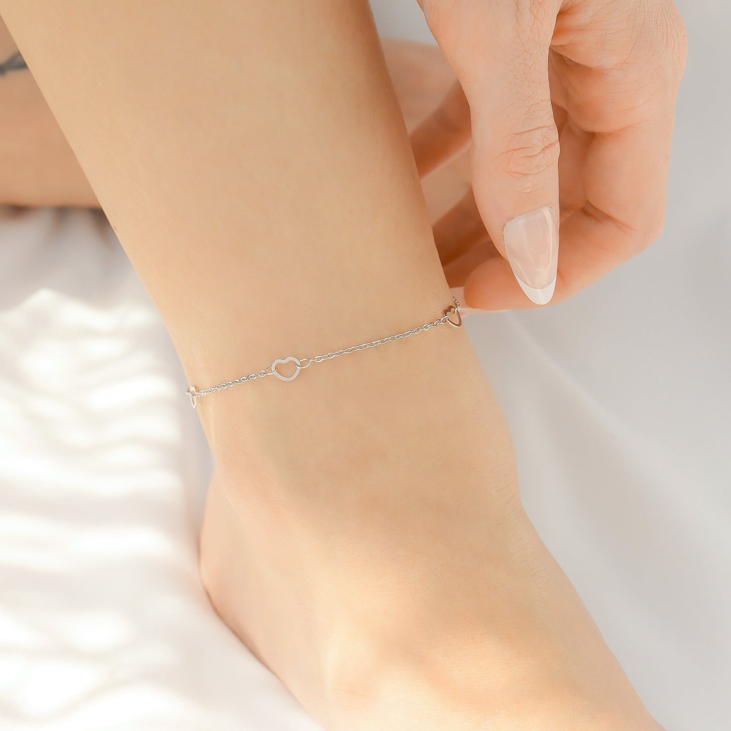 Silver anklet with evenly spaced hearts on a person's ankle with a blurred background