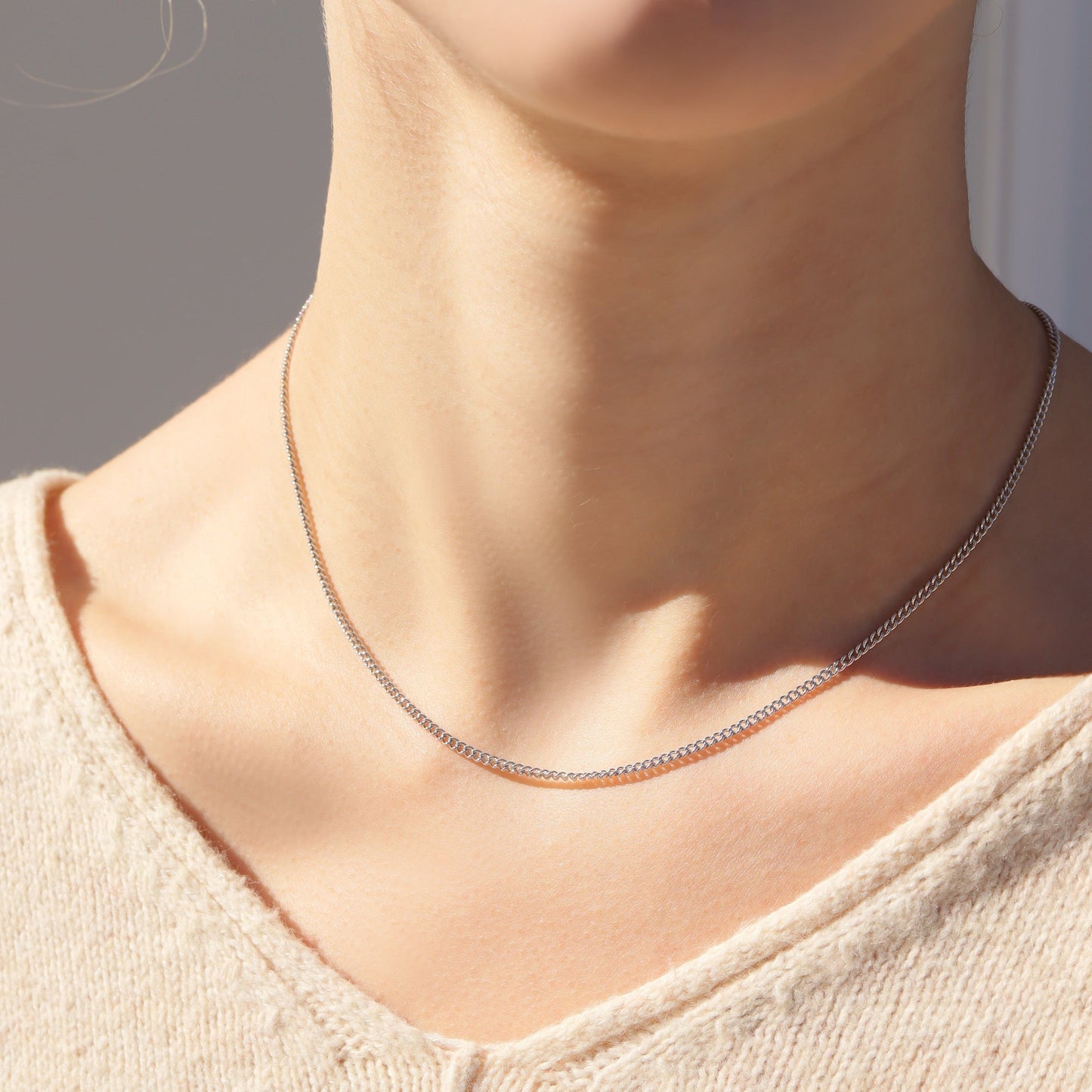 Close-up of a person wearing a delicate silver necklace against a neutral background