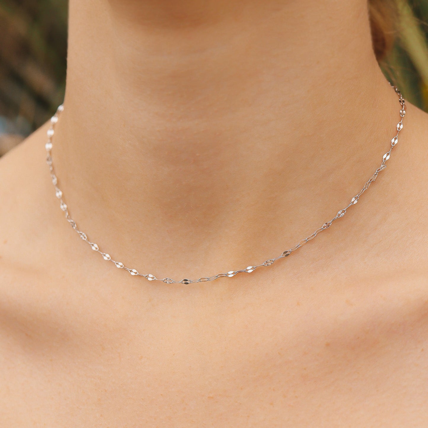 Silver necklace on a person's neck with a blurred natural background