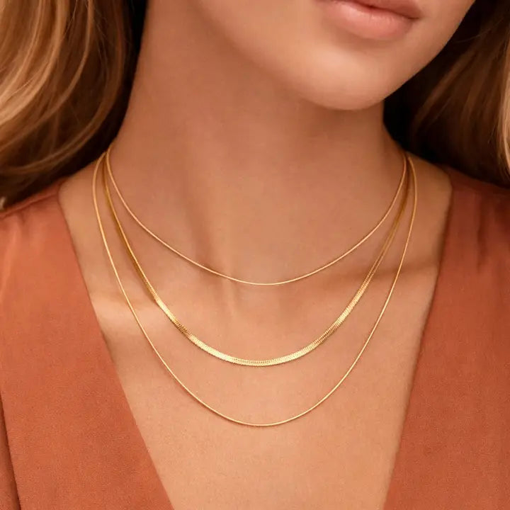 Three gold necklaces on a person wearing a rust-colored top.