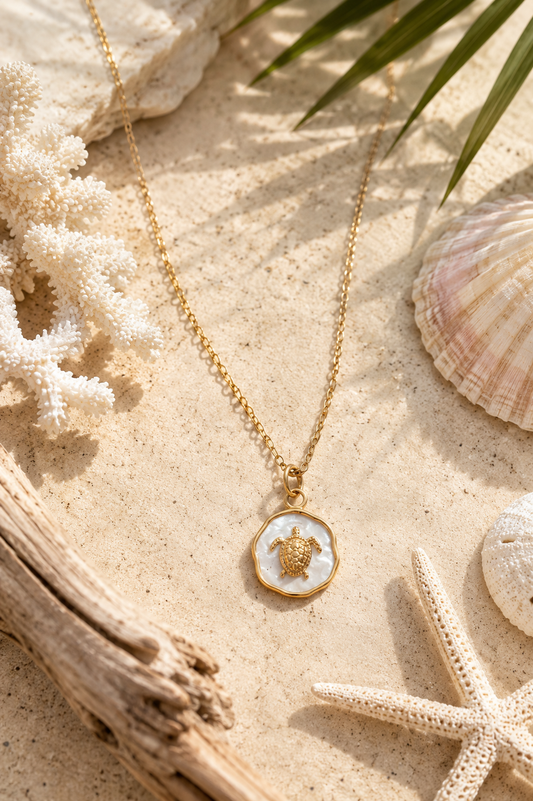 Gold chain with sea turtle pendant lying in beach background.