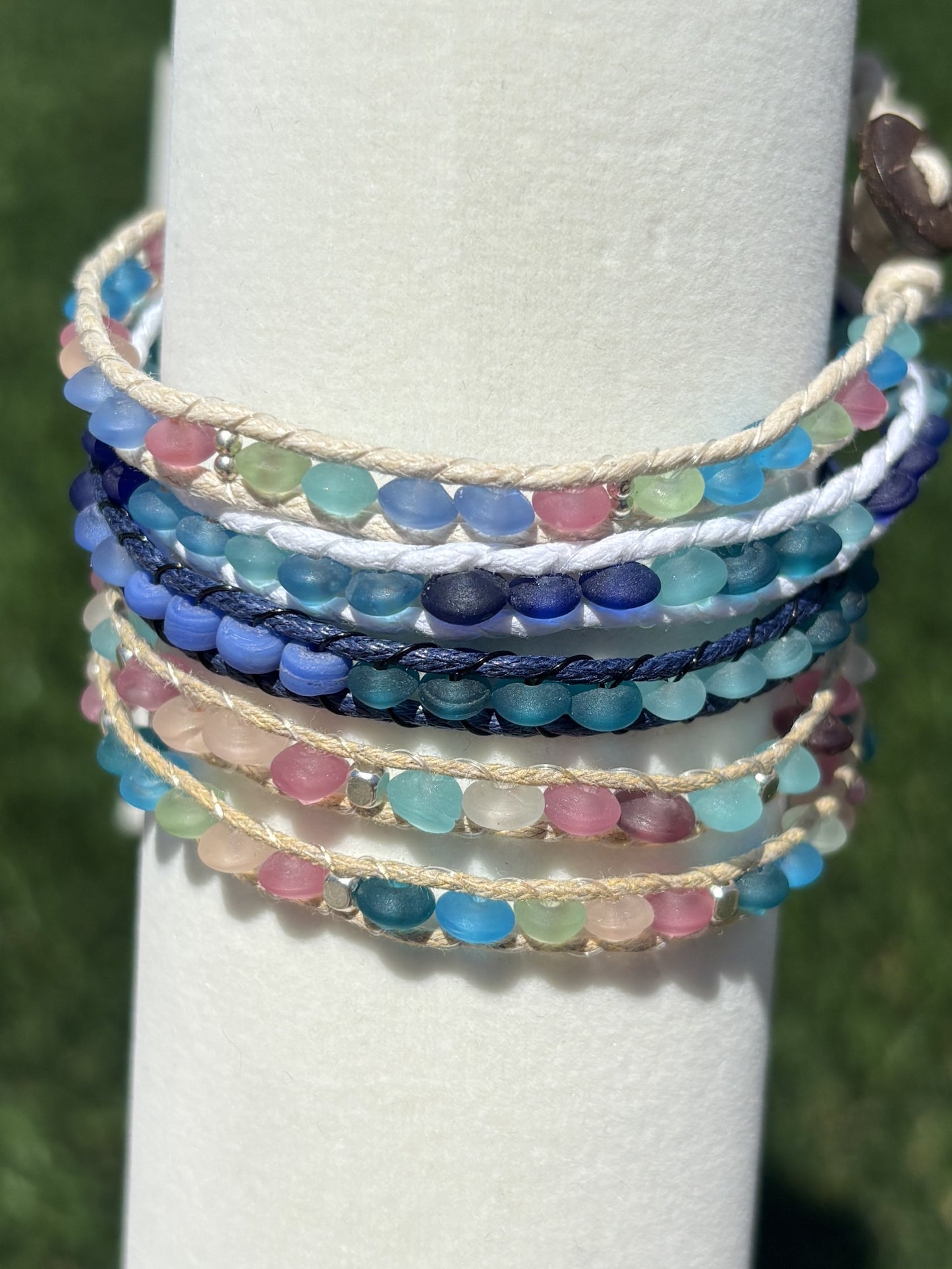 Stack of colorful beaded bracelets on a white cylindrical stand with a blurred green background