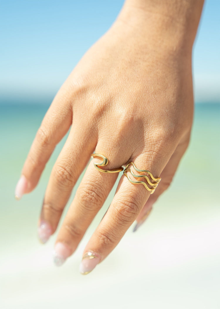 Close up of a woman's hand with two gold rings on it with a blurred beach background