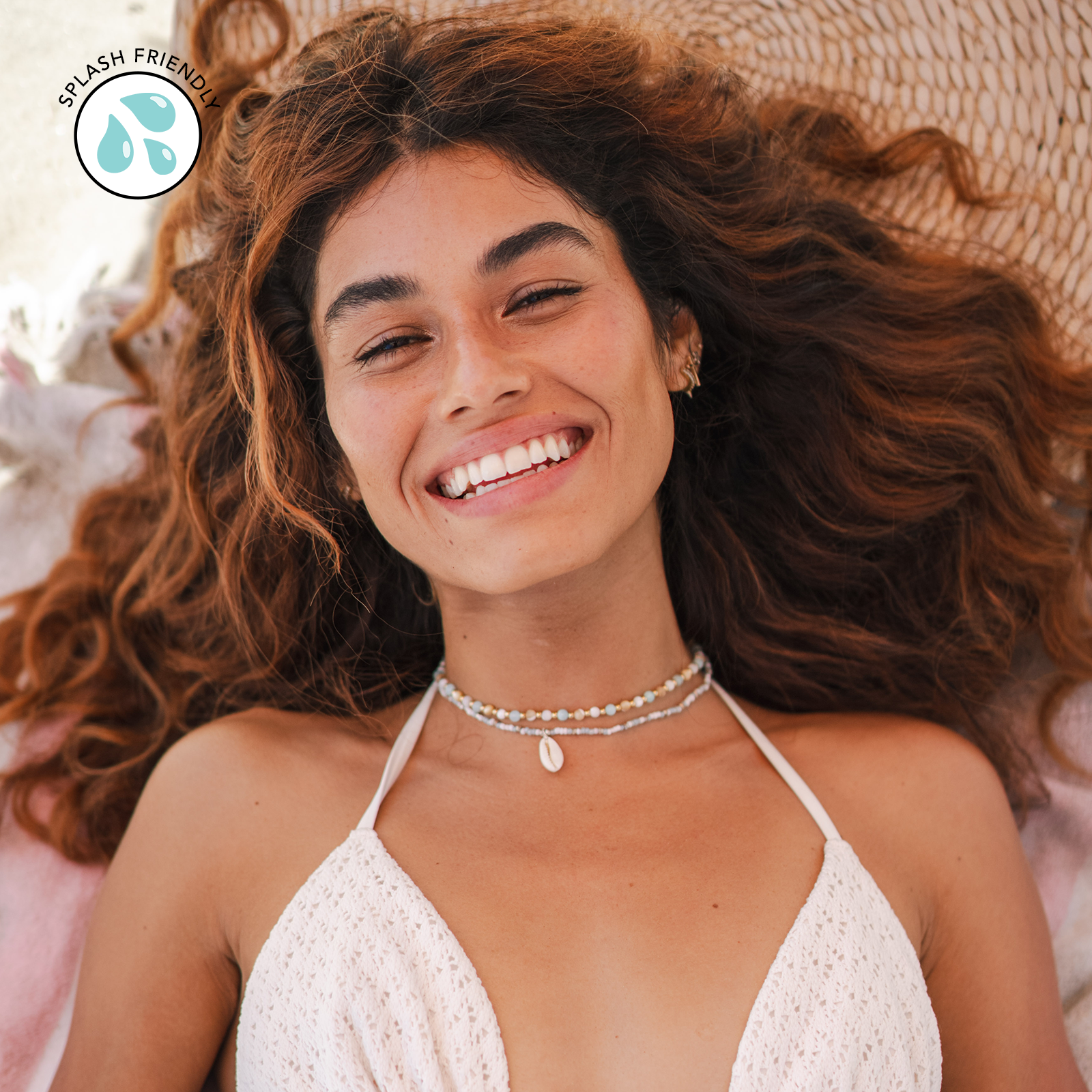 Woman with long, wavy hair wearing a white bikini top, lying on a textured surface.