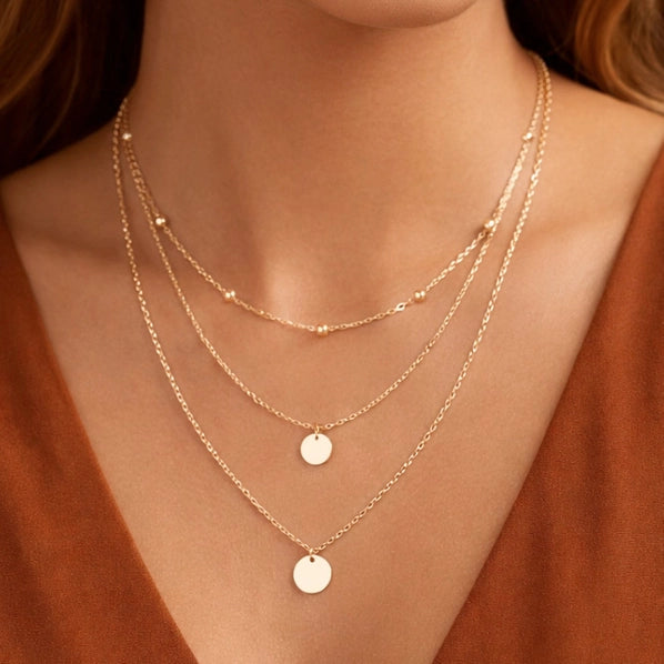 Layered gold necklaces on a person wearing a rust-colored top.