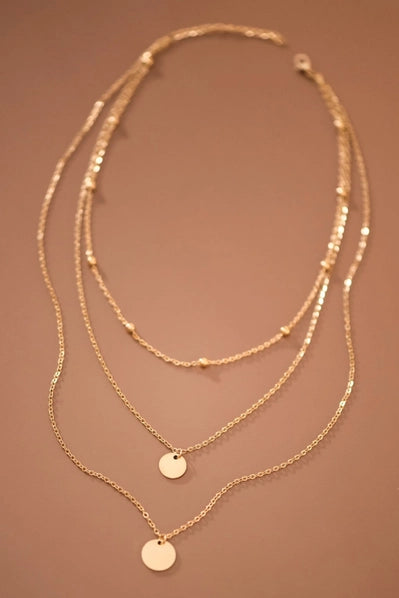Three gold necklaces with circular pendants on a brown background