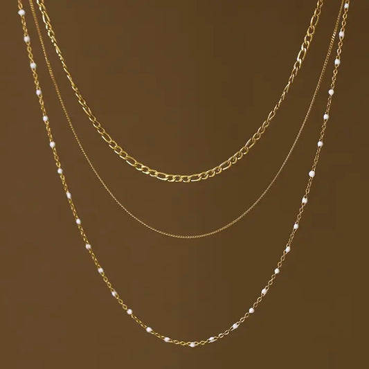Three gold chains with small white beads on a brown background