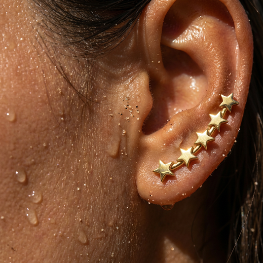 Close-up of an ear with gold star-shaped ear climber earrings on a wet skin background