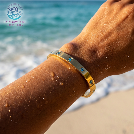 Gold bracelet with blue stones on a person's wrist by the ocean