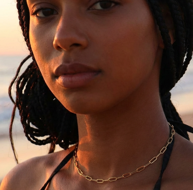 Woman wearing a gold chain necklace on a beach at sunset