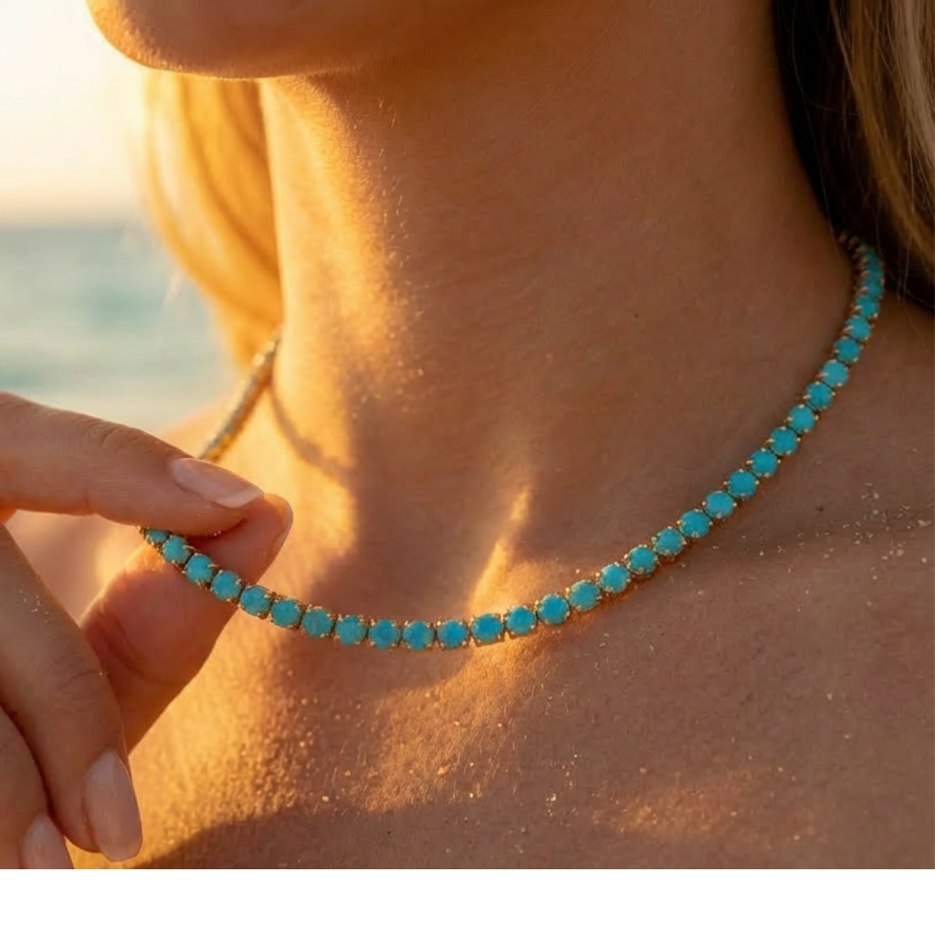 Turquoise rhinestone and gold tennis necklace being worn with a blurred beach background