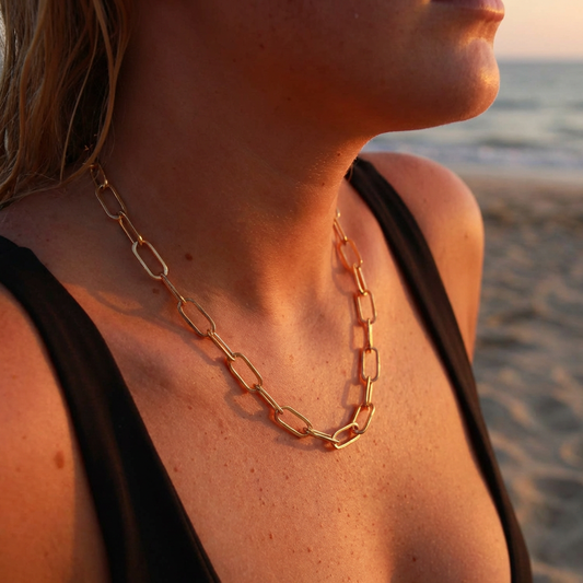 Person wearing a large link paperclip chain necklace with a black swimsuit on a beach at sunset