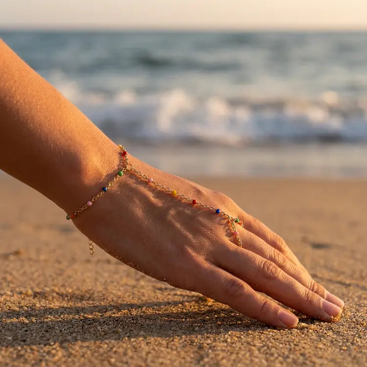 Hand with colorful beaded hand chain on a sandy beach with ocean waves in the background