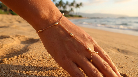 Hand wearing a gold hand chain on a beach with ocean and palm trees in the background