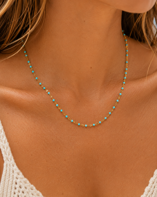 A delicate gold chain necklace with small turquoise blue beads, worn on a model's neck.