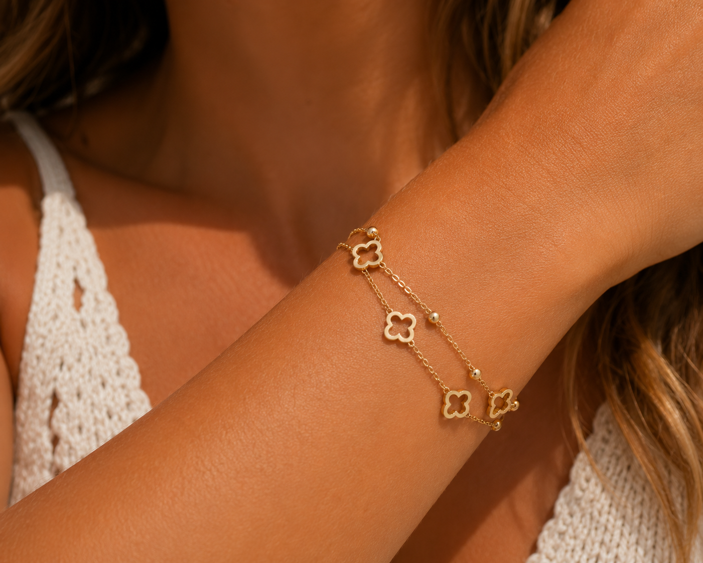 A delicate gold chain bracelet with four interconnected clover motifs worn on a woman's wrist, shown in a warm, close-up lifestyle shot.