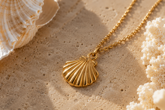 Gold chain with seashell pendant lying on a cream-colored background near shells.
