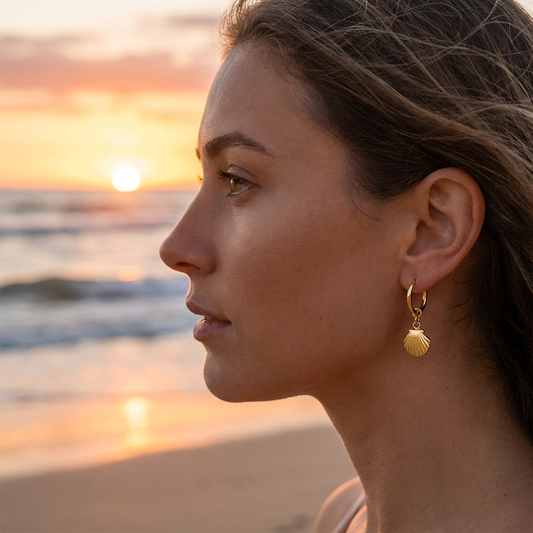 Woman wearing a shell-shaped earring with a sunset over water in the background
