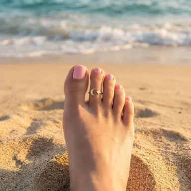 Foot with a moon and star toe ring on a sandy beach with ocean waves in the background