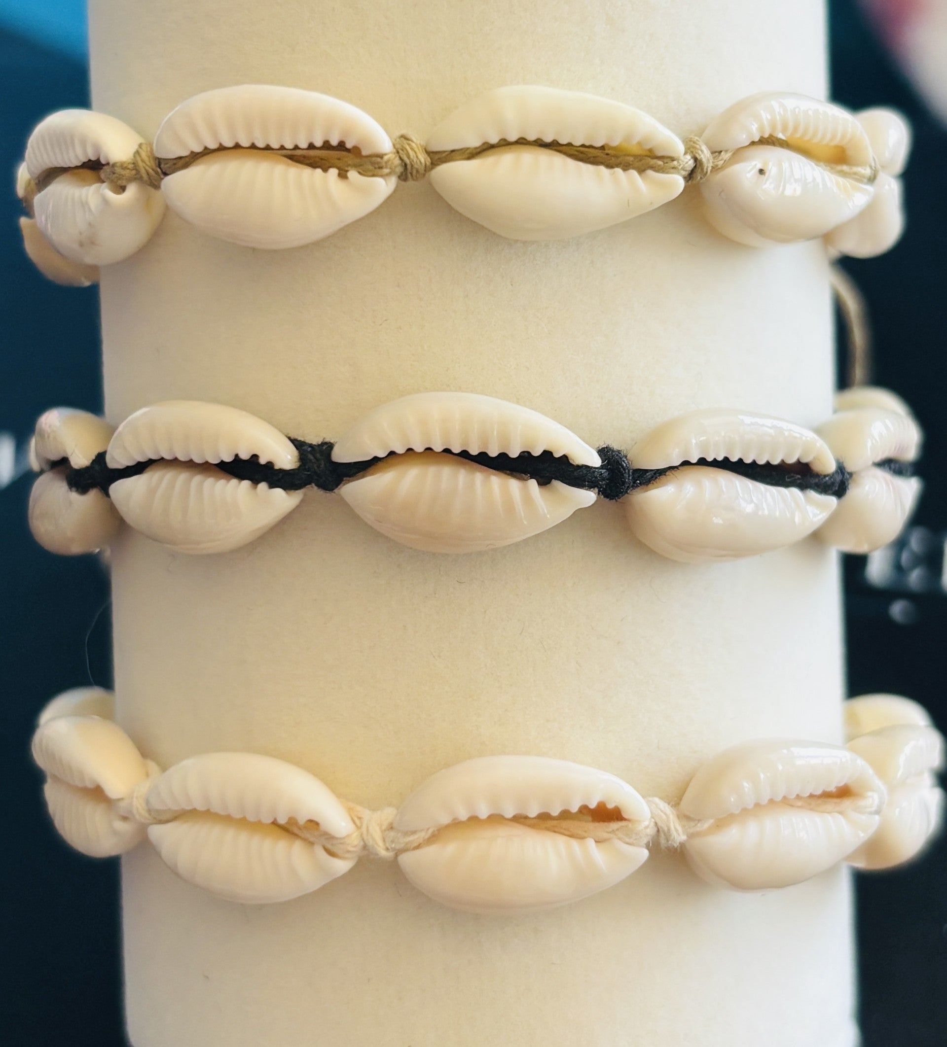 Three Cowrie Shell Bracelets close up on a white cylindrical stand