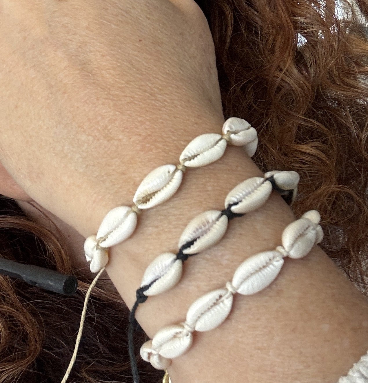 Close-up of a wrist wearing three different color cowrie shell bracelets