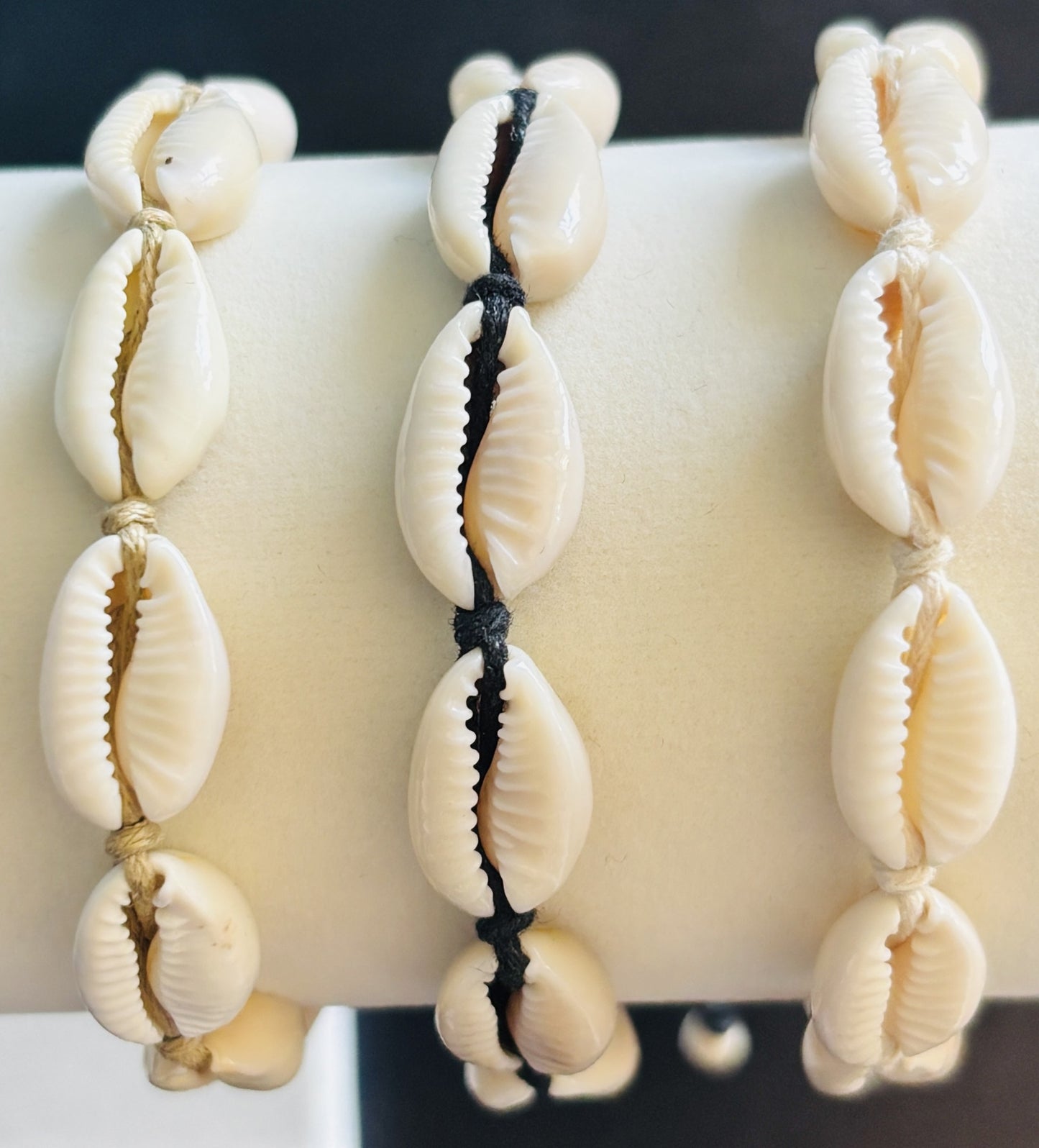 Close up of three cowrie shell bracelets on a white bracelet stand