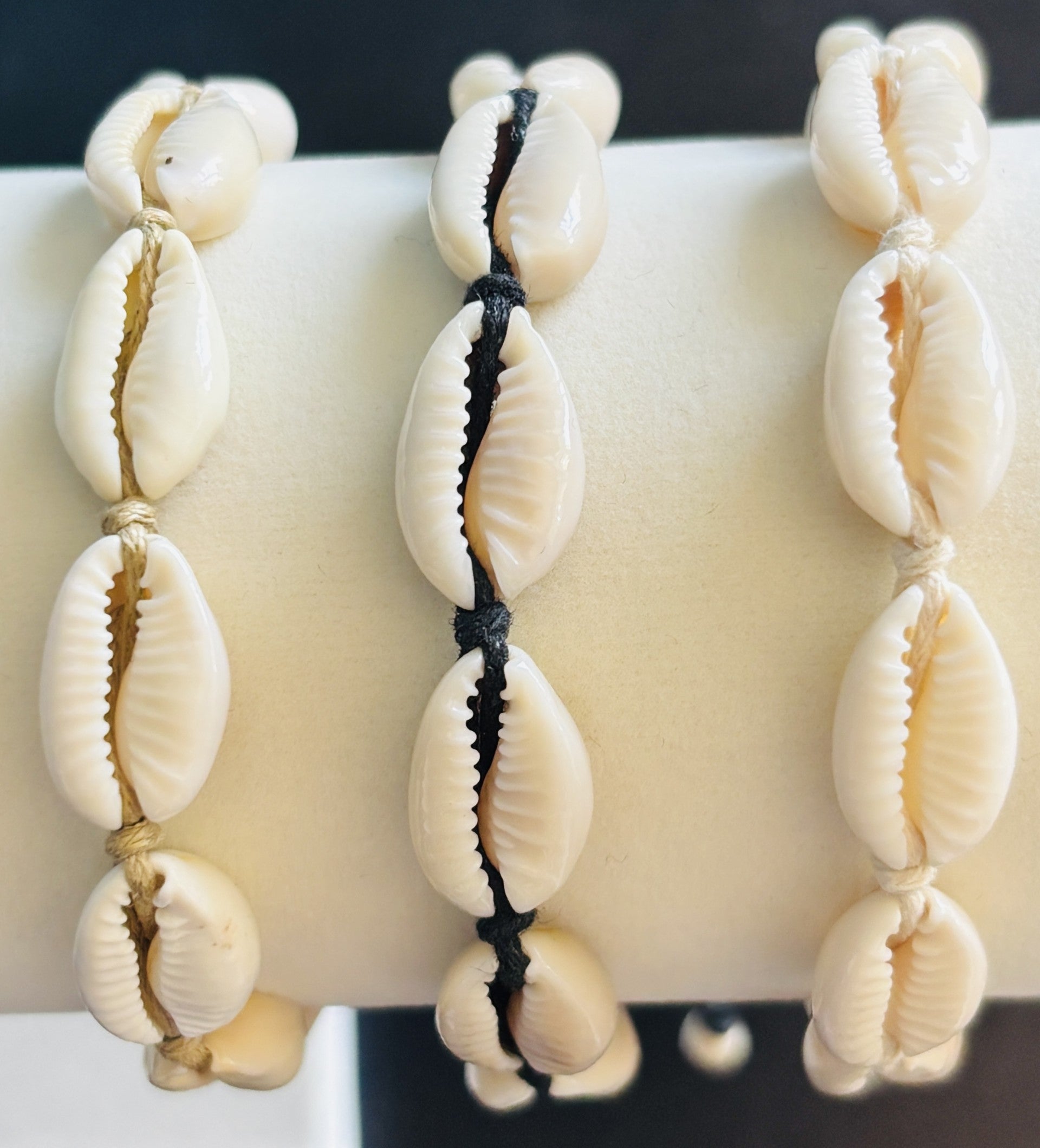 Close up of three cowrie shell bracelets on a white bracelet stand