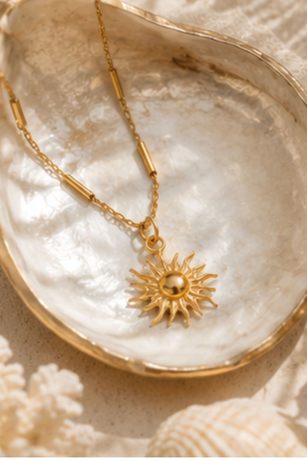 Gold bar station chain with sun pendant lying in an open clam shell on a shiny white surface.