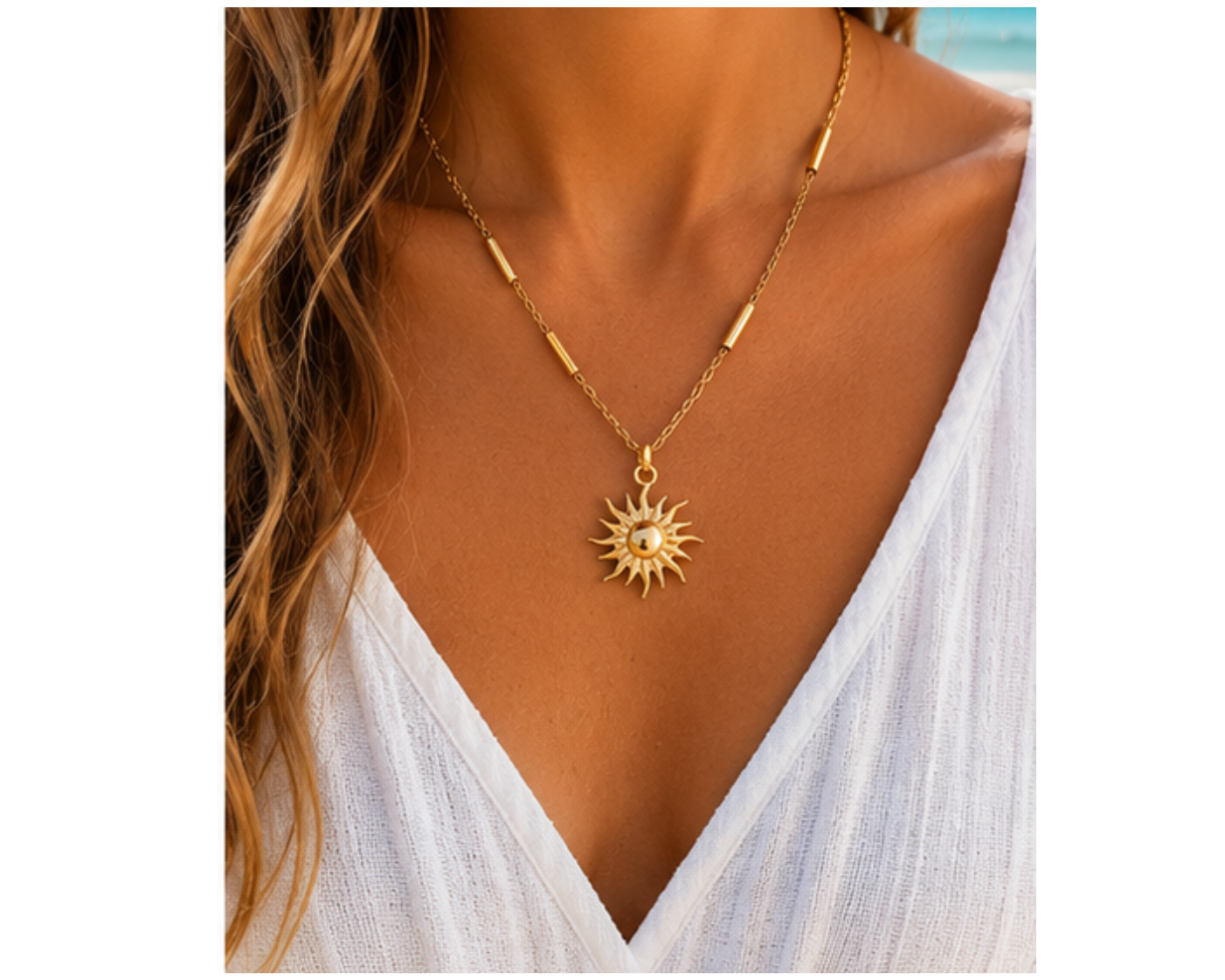 Woman with long brown wavy hair in a white dress wearing a gold bar station necklace with sun pendant.