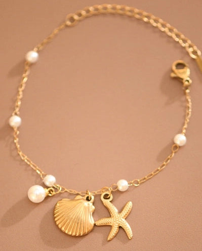 Gold bracelet with shell and starfish charms on a brown background