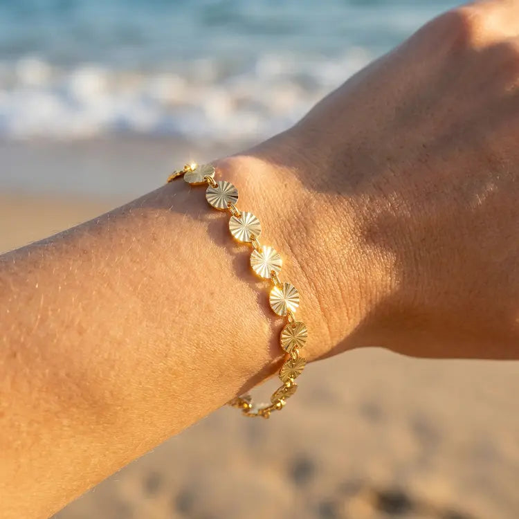 Gold bracelet with mini sun shapes on a wrist with a beach background