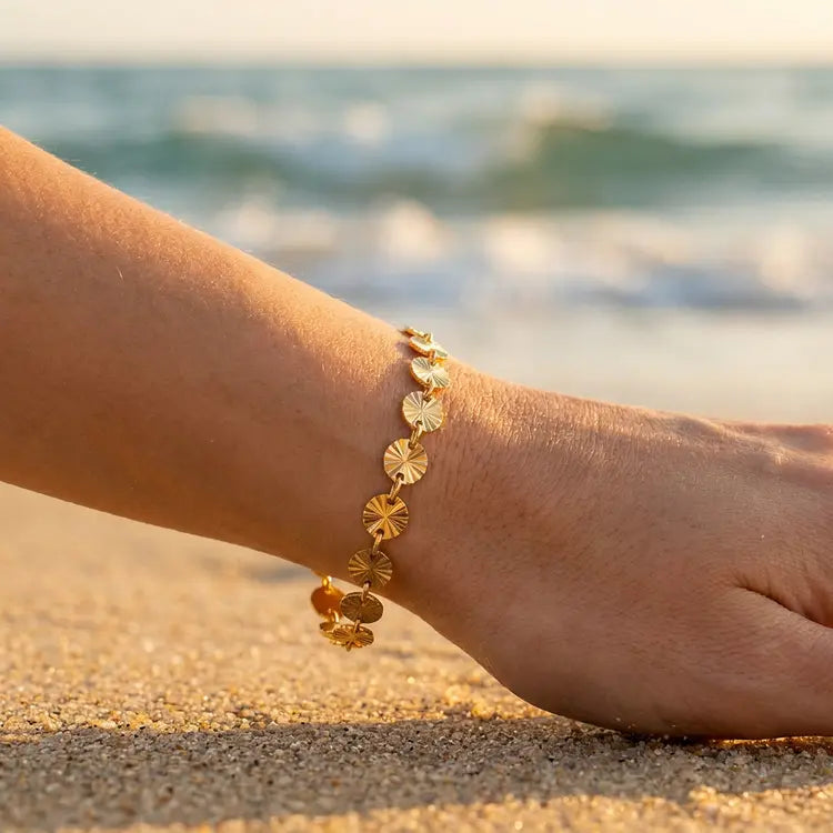 Gold bracelet on a person's wrist with small sun shapes with a blurred beach background