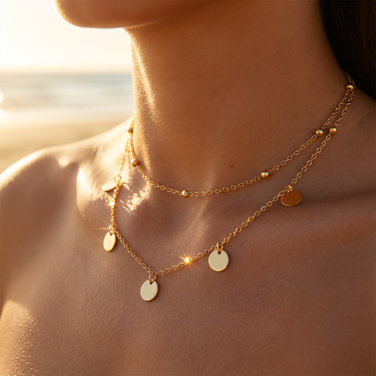 Close-up of a person wearing a gold layered necklace with circular pendants against a blurred natural background.