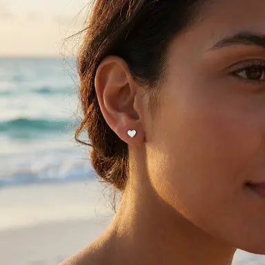 Heart-shaped earring worn by a person with a beach background
