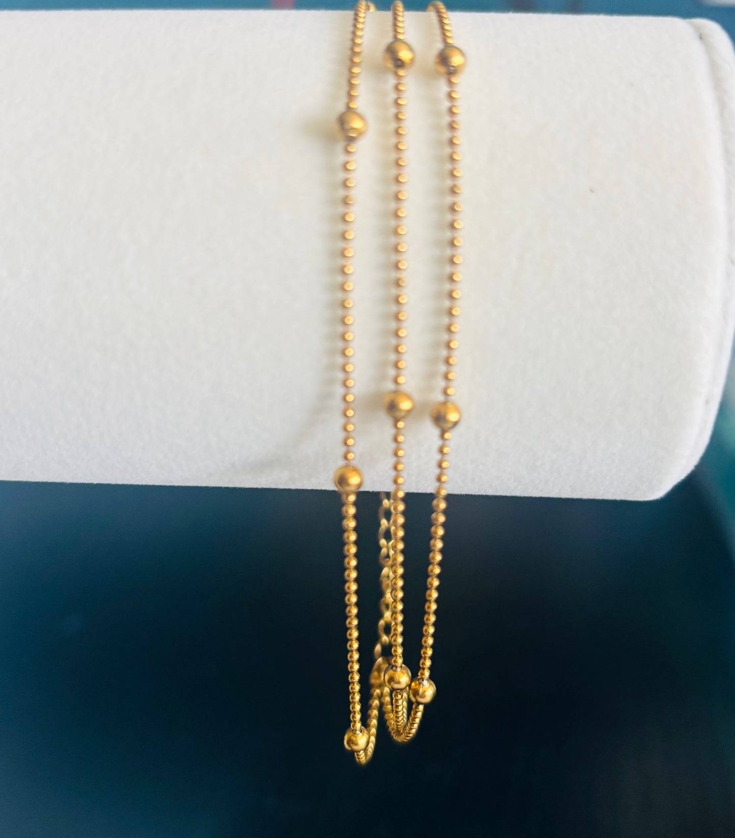 Gold beaded bracelet on a white cushion with a blue background