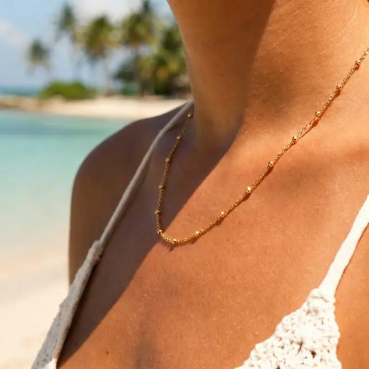 Person wearing a gold necklace with a beach and palm trees in the background