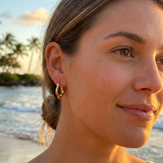 Woman with flower design gold hoop earrings on a beach at sunset