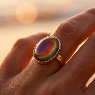 Ring with a colorful stone on a hand against a blurred sunset background