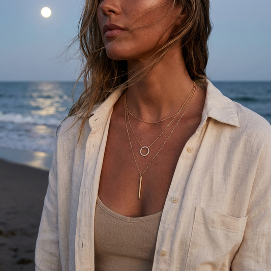 Woman on a beach wearing layered necklaces with a moonlit sky.