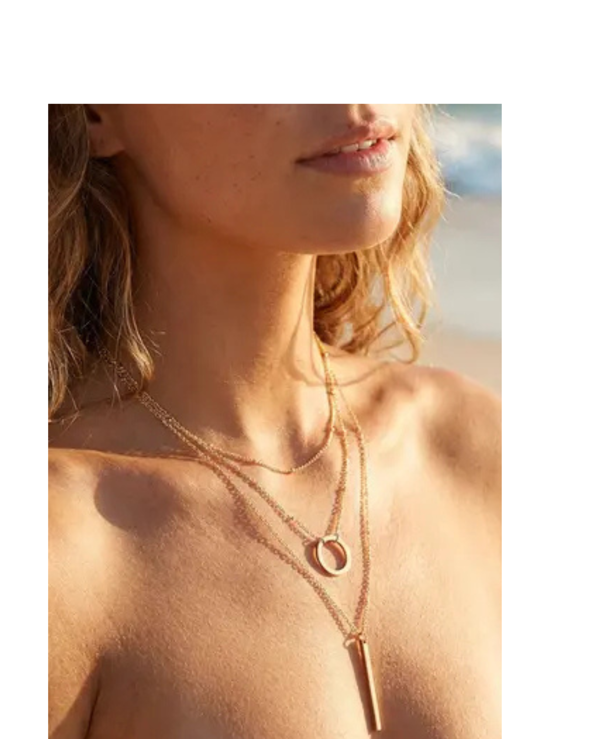 Close-up of a person wearing a gold three layered necklace with a beach in the background