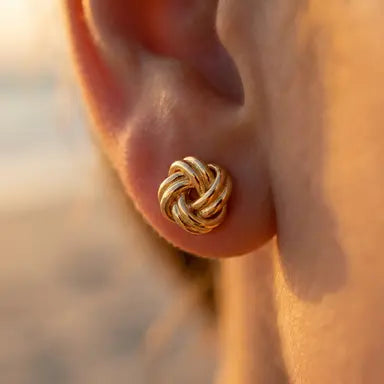 Gold knot earring worn on an ear with a blurred background