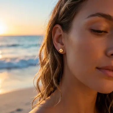 Woman wearing gold knot earrings with a beach and sunset in the background